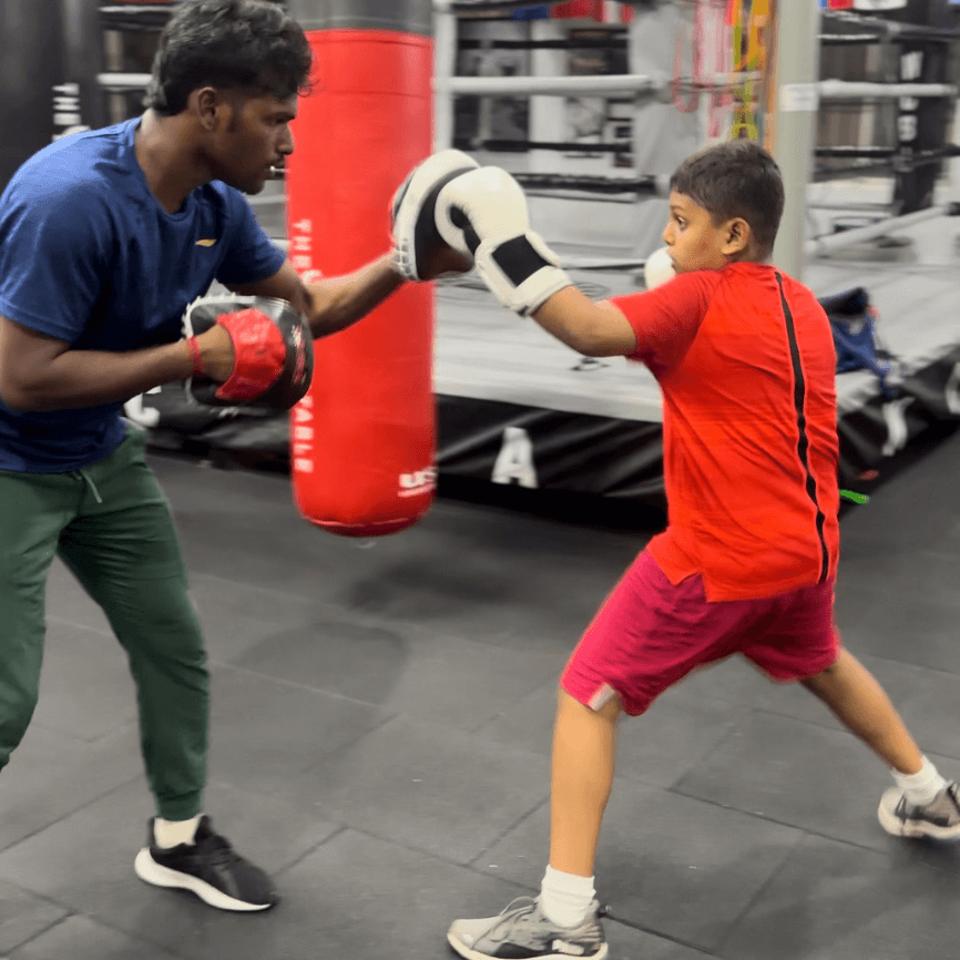 Young beginner learning proper boxing technique with coach, focusing on jab and form over power in boxing classes.