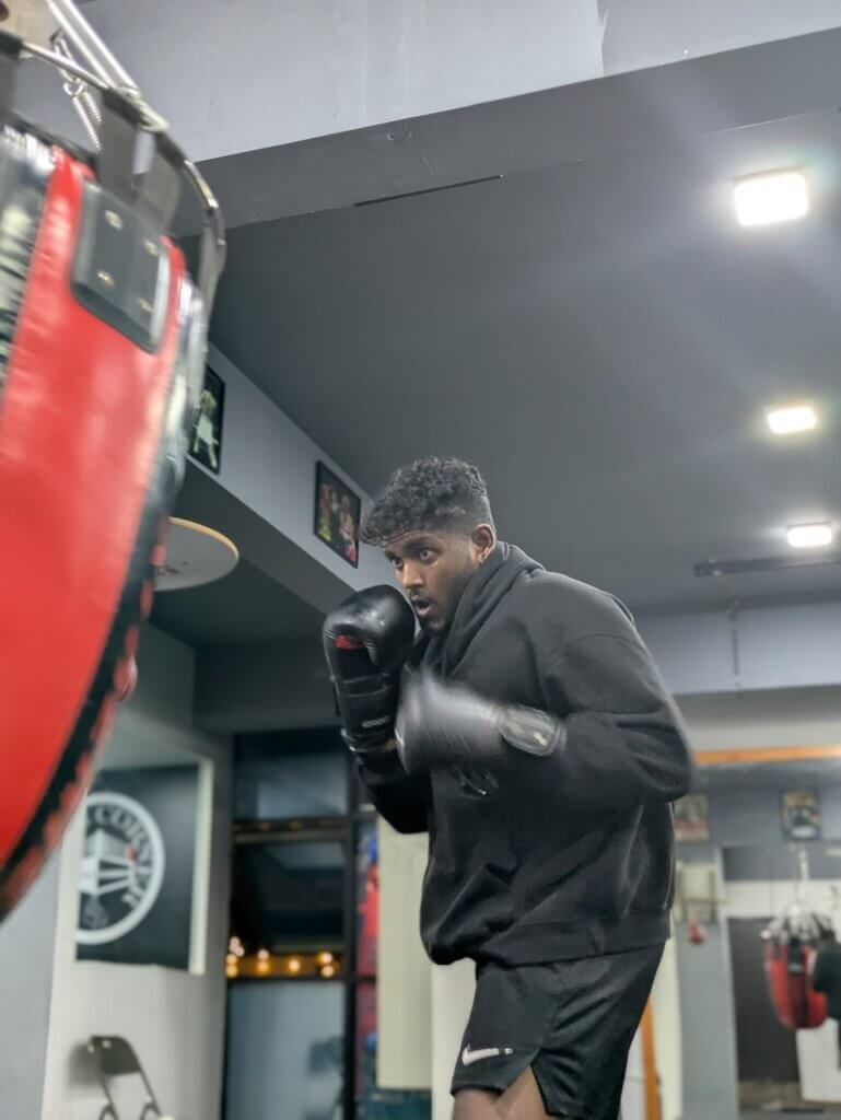 Boxer in black hoodie training on heavy bag at White Corner Boxing gym for fat loss and fitness in Bangalore